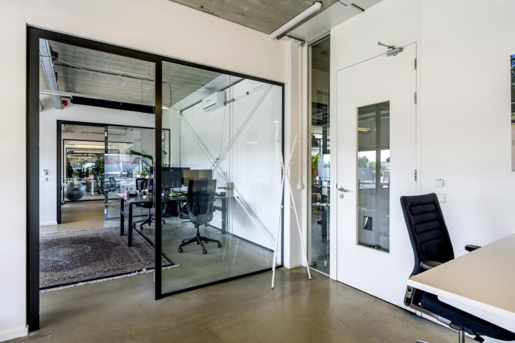 Modern office interior on Johan van Hasseltweg with glass walls, minimalist furniture, and an industrial ceiling.